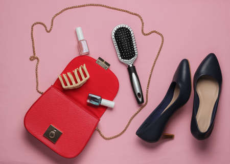 What's in women bag. Red leather bag with women's accessories, cosmetics products, high heel shoes on pink background. Minimalistic fashion concept. Studio shotの写真素材
