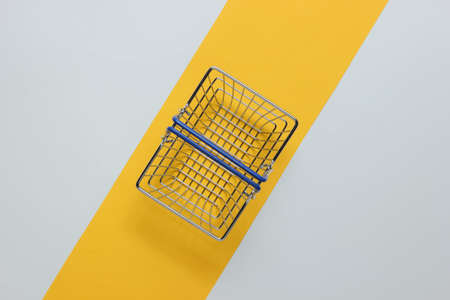 Minimalistic shopping concept. Shopping basket on white-yellow background.の写真素材