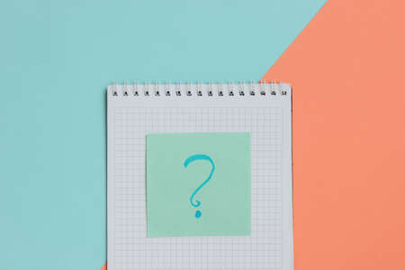 Notepad and memo piece of paper with question mark on pink blue background.
