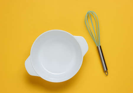 Cooking concept. Empty white bowl with whisk on yellow studio background. Top view.の写真素材