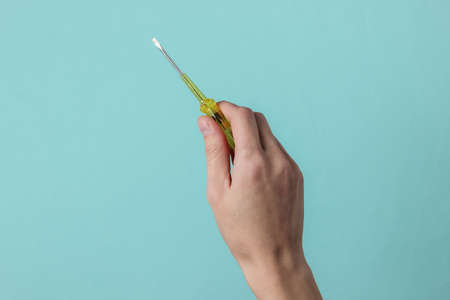 Repair concept. Female hand holds a screwdriver on a blue studio background.の写真素材