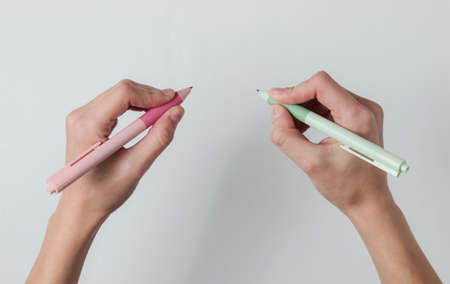 Ambidextr. Female hands hold pens and write on white background. Top view. Studio shot