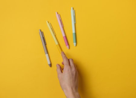 Female hand selects pen on yellow background. Top viewの写真素材