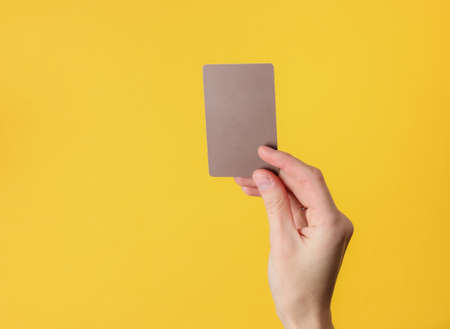 Female hand holds a blank brown business card on yellow backgroundの写真素材