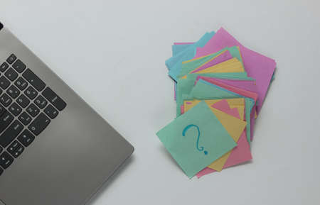 Minimalistic office concept. Lptop and lot of memo papers with question mark on white background. Top viewの写真素材