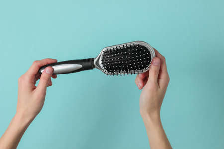 Female hands hold comb on blue background. Hair care. Beauty concept
