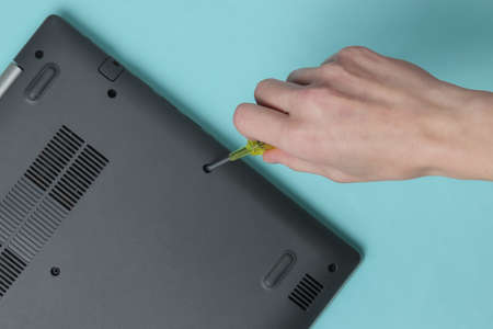 Service center. Laptop Repair. Female hand screwdriver unscrews laptop bolts on blue background