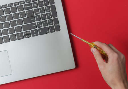 Service center. Laptop Repair. Hand holds a screwdriver near a laptop on a red background