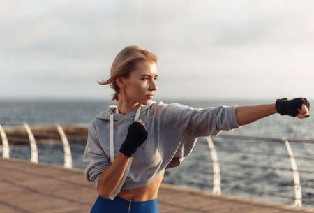 Young woman kickboxer with wrapped hands in bandages trains punch on the beach at sunrise. Morning training fighterの写真素材