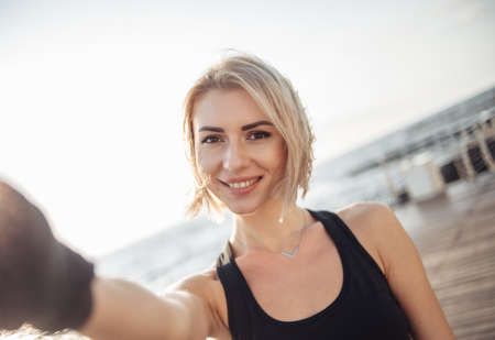 Selfie portrait of a young cheerful fitness woman on the beach at sunrise