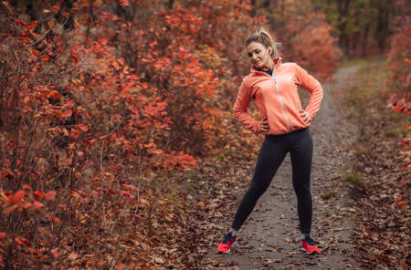 Young attractive sport woman in sportswear doing stretching exercise in autumn forest with reddened leaves of trees. Warm up before training. Healthy lifestyle conceptの写真素材