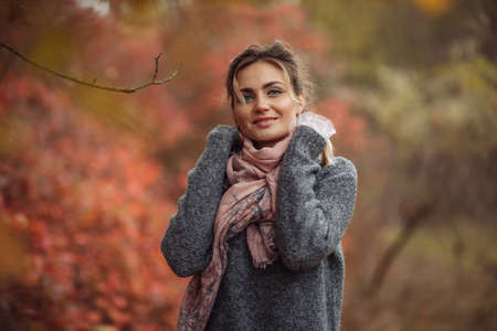 Art portrait. Young cheerful woman in autumn clothes posing in a forest with reddened leaves of treesの写真素材