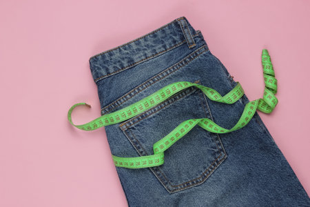 Blue Jeans with measuring tape on pink background. Concept of weight loss, diet, detox. Top viewの写真素材