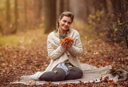 Art portrait. Young attractive woman sits on a plaid and holds fallen leaves in her hands in the...