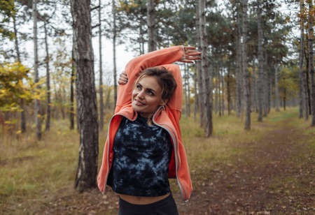 Young attractive sport woman in sportswear doing stretching exercise for hand in autumn forest. Warm up before jogging. Healthy lifestyle conceptの写真素材