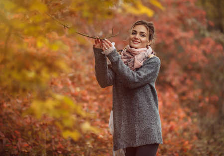 Art portrait. Young cheerful woman in autumn clothes posing in a forest with reddened leaves of treesの写真素材