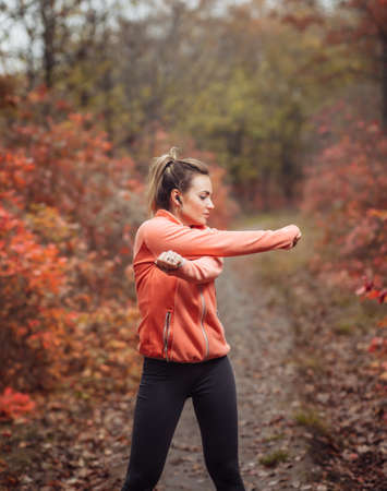 Young attractive sport woman in sportswear doing stretching exercise for hand in autumn forest with reddened leaves of trees. Warm up before training. Healthy lifestyle conceptの写真素材