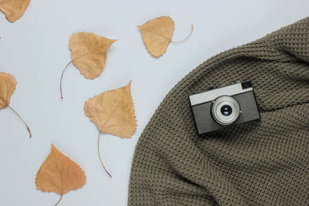 Knitted sweater with a retro camera and fallen leaves on white background. Autumn time. Top viewの写真素材