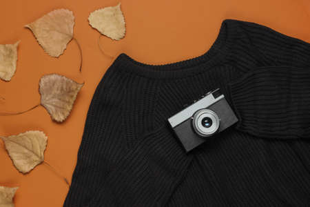 Black sweater with a retro camera and fallen leaves on brown background. Autumn time. Top viewの写真素材