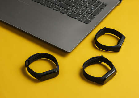 Laptop and sart bracelets on a yellow background. Modern gadgets. Top viewの写真素材