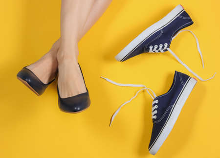 Female legs in classic high heel shoes on a yellow background with sneakers. The choice between...