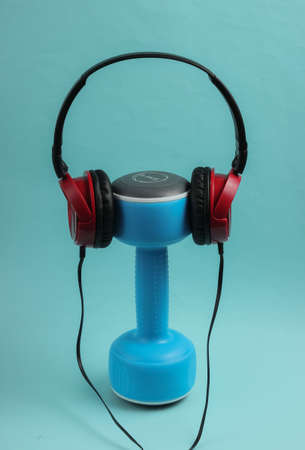 Minimalistic sport and fitness concept. Wired headphones and  dumbbell on blue  background