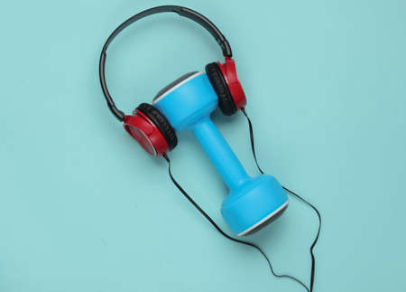 Minimalistic sport and fitness concept. Wired headphones and  dumbbell on blue  backgroundの写真素材