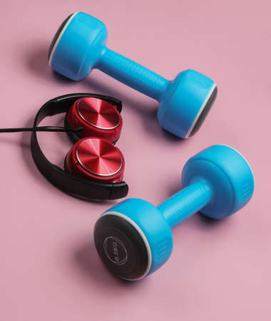 Minimalistic sport and fitness concept. Wired headphones and  dumbbell on pink  background.の写真素材