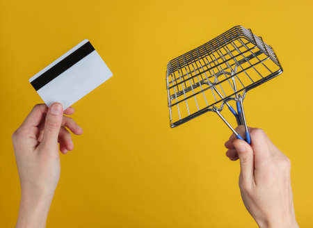 Female hand holds a bank card and shopping basket on yellow background. Online Shopping Conceptの写真素材