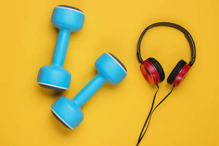 Minimalistic sport and fitness concept. Wired headphones and  dumbbell on yellow  backgroundの写真素材