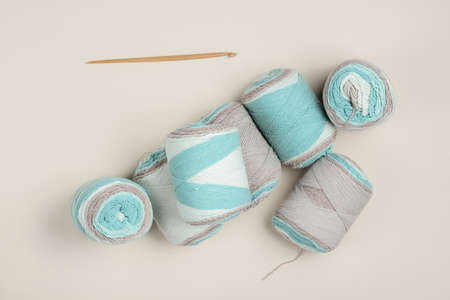 Woolen skeins of thread and crochet hook on a beige background. Top view