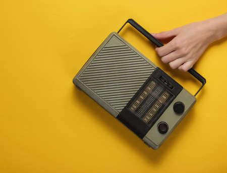 Female hand holds a retro radio receiver on a yellow background. Retro Mass Media, 70s. Ð¡Ð²ÐµÑÑÑ Ð²Ð¸Ð´の写真素材