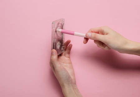 Female hands rewind an audio cassette tape on a pink pastel background. Analog technology of the...
