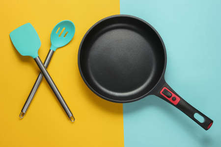 Non-stick pan with cooking spatula on blue yellow background. Cooking minimalism concept. Studio shot. Top viewの写真素材