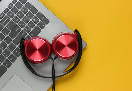 Laptop and dj headphones on yellow pastel. Top view