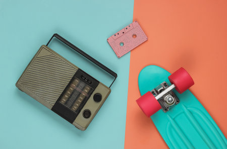 Overhead view of cruiser board, radio receiver, audio cassette on a blue-pink pastel background. Summer fun, 80s retro style, pop culture. Top viewの写真素材