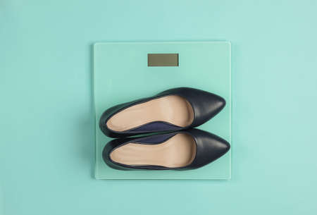 Women's classic high-heeled shoes on floor scales. Blue studio background. Slimming concept. Top viewの写真素材