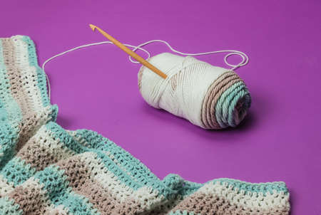 Skein of wool threads with yarn and wooden crochet hook on purple background. Hobbies