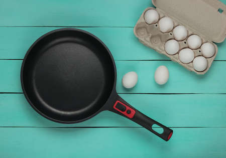 Non-stick pan and tray of eggs on blue wooden background. Top viewの写真素材