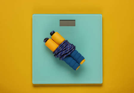 Floor scales, skipping rope on a yellow background. Slimming concept, fitness training. Studio shot....