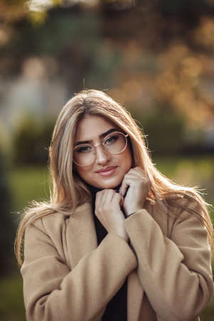 Autumn portrait. Cheerful stylish woman in image glasses and coat in the park
