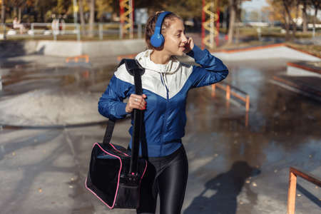 Young fit woman in sportswear with a bag and headphones walking in a sports park.の写真素材