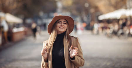 Young happy woman dressed in a coat and felt hat walks around the city. Autumn timeの写真素材