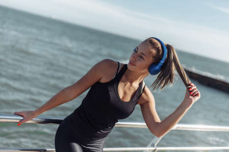 Relaxed fit woman in sportswear with headphones listen to music on the beach at bright sunny dayの写真素材