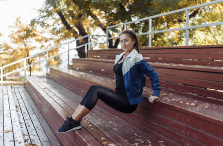 Fit slim woman practices reverse push-ups for hands from wooden stands. Outdoor training