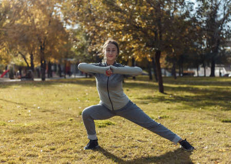 Aerobics workout outdoors. Young sport woman in sportswear is training in the autumn park.