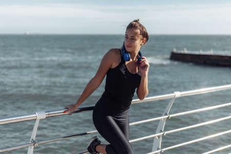Relaxed fit woman in sportswear with headphones listen to music on the beach at bright sunny dayの写真素材