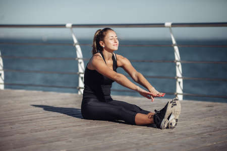 Slim fit woman in sportswear doing stretching legs on the beach at bright sunny dayの写真素材