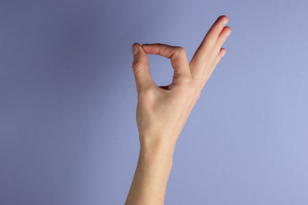 Female hand shows okay gesture on purple backgroundの写真素材