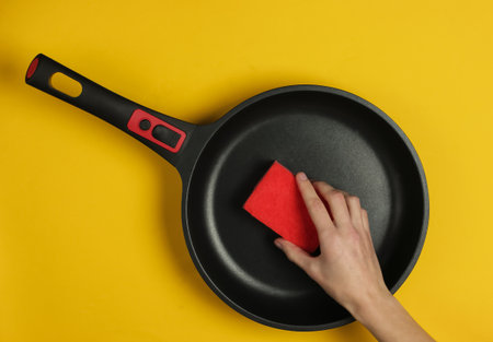 Woman washes pan with sponge on yellow background. Studio shot. Top viewの素材 [FY310171758587]